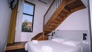 Quarto com escada de madeira, cama com roupa de cama branca e janela com cortinas.