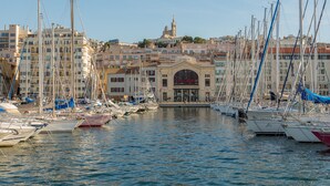Uma marina com vários veleiros atracados, um edifício em destaque com uma placa indicando "LA CRÉE" e uma torre ao fundo.