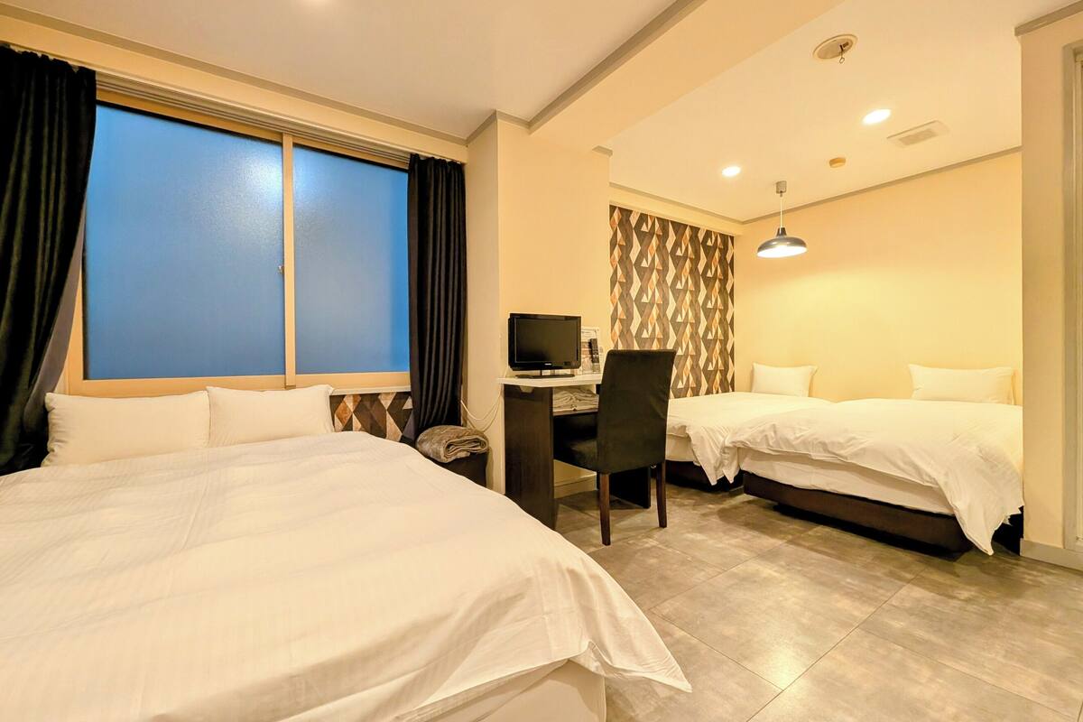 Habitación de hotel con dos camas, un escritorio con computadora y un ventanal con cortinas.