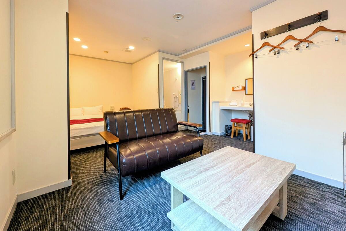 Habitación de hotel compacta con sofá de cuero, una mesa de madera y un taburete pequeño.
