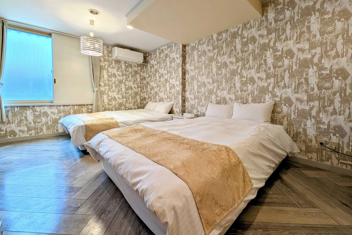 Habitación de hotel con dos camas, un ventanal grande y un papel pintado estampado.