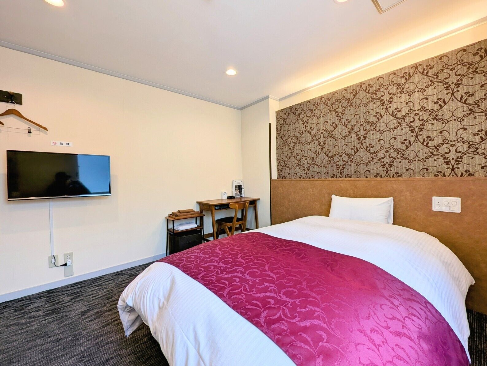 Una habitación de hotel con cama, escritorio, silla, televisor y pared con diseño.