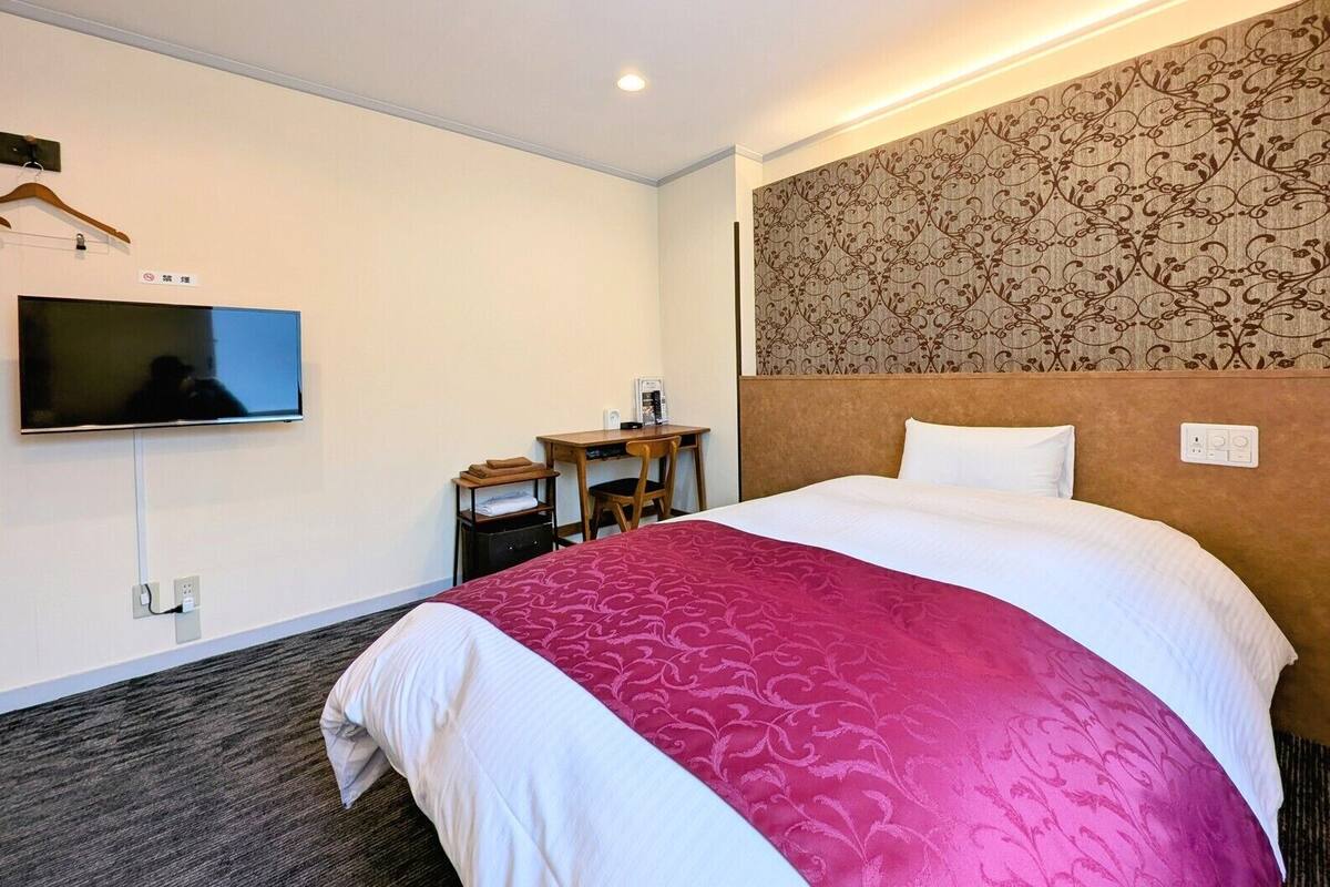 Una habitación de hotel con cama, escritorio, silla, televisor y pared con diseño.