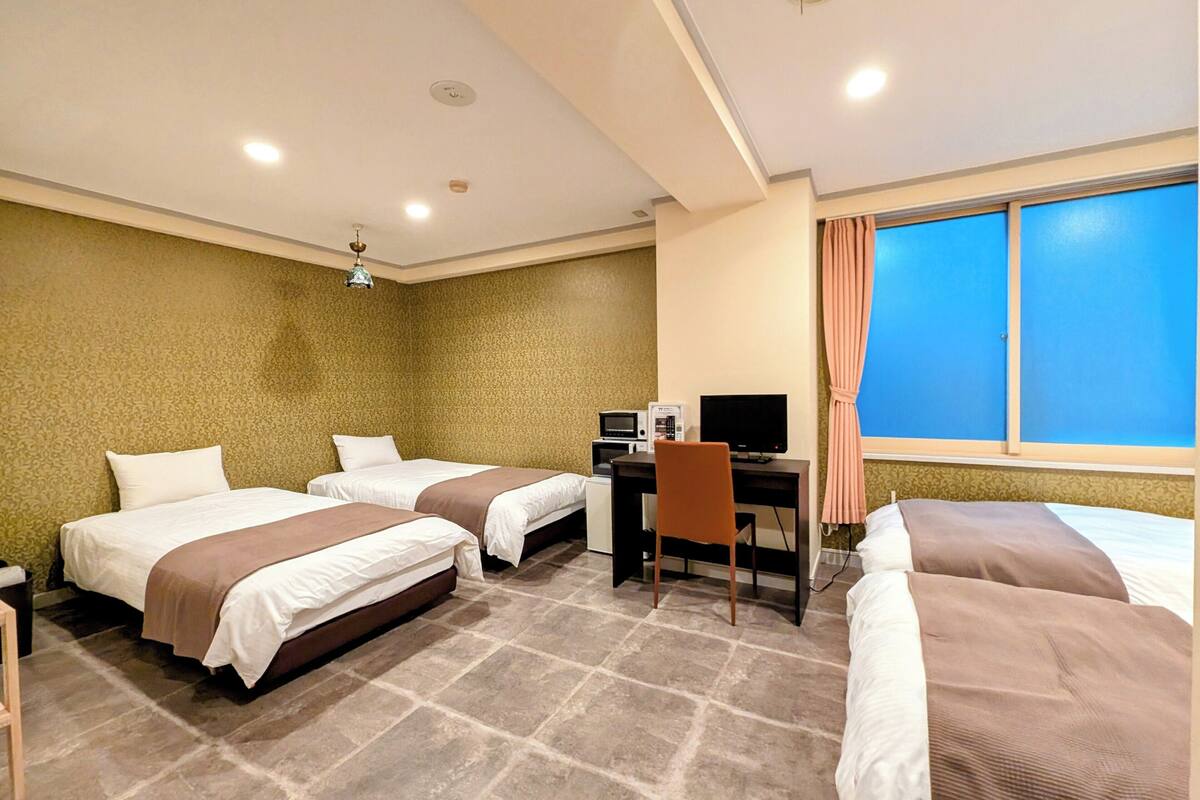 Habitación de hotel con dos camas, un escritorio con computadora, una ventana con cortinas y una pared con diseño.