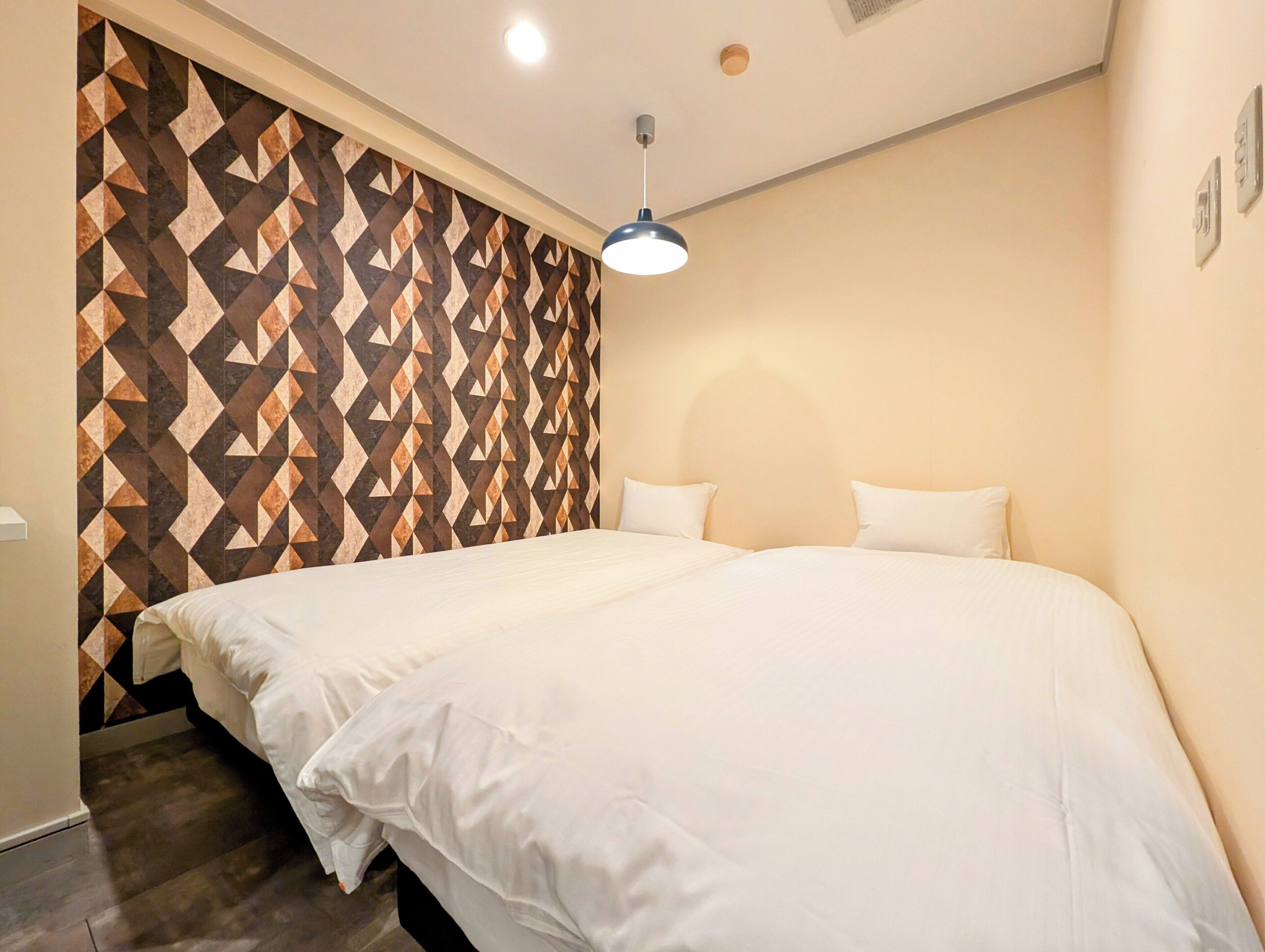 A hotel room with a large bed, a geometric-patterned wall, and a ceiling light.