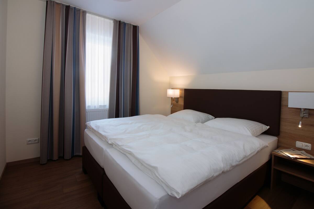 A hotel room with a large bed, a bedside lamp, and a window with curtains.