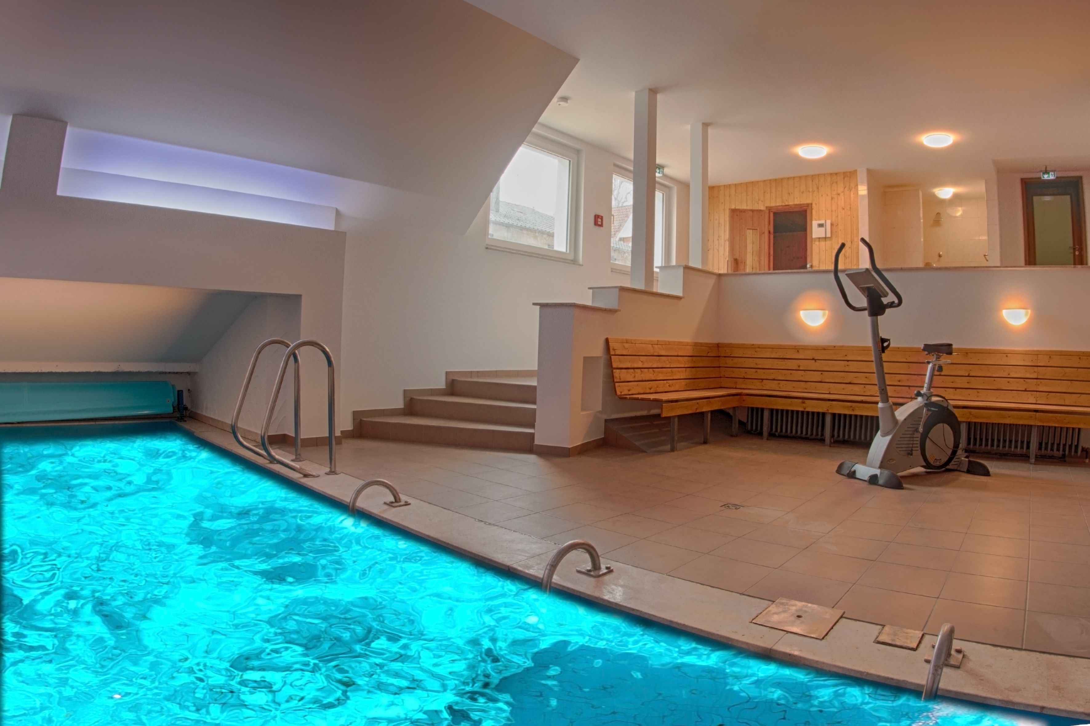 Ein Schwimmbecken mit Stufen, die zu einer Holzbank und einem Fitnessrad führen.