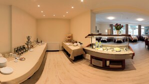 Comedor de hotel con barra de buffet, un radiador y vista del área de comidas al fondo.