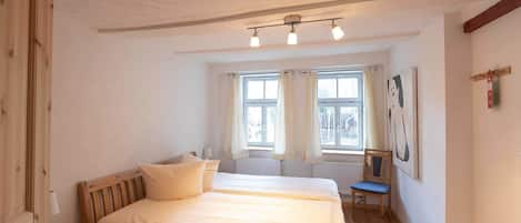 Ein Schlafzimmer mit einem Bett, einem Sessel, einem Fenster mit Vorhängen und einem Bild an der Wand.