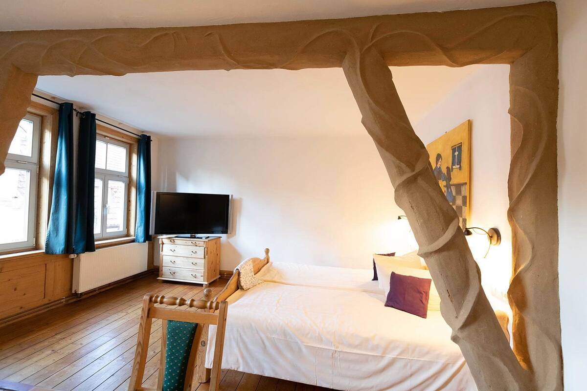 Une chambre à coucher avec un lit, une télévision, une commode et une fenêtre avec des rideaux.