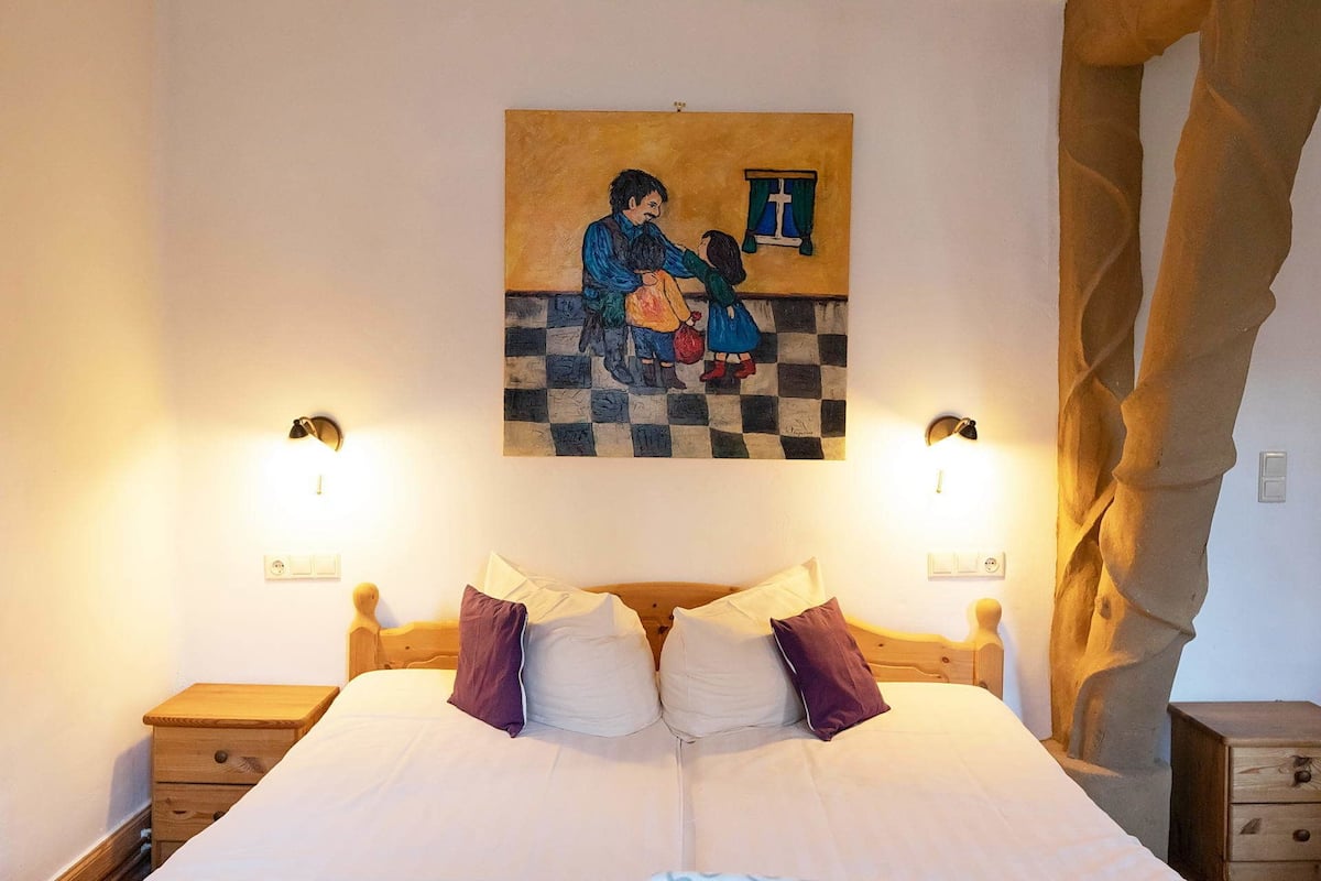 Une chambre avec un grand lit, deux tables de chevet, un tableau accroché au mur et un sol à carreaux.