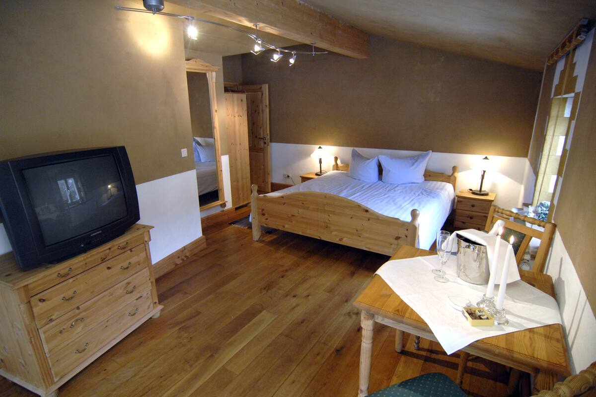 Une chambre à coucher avec un lit en bois, un téléviseur posé sur une commode en bois, une petite table avec des bougies et une table de chevet en bois.