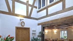 Un comedor con mesas y sillas de madera, un reloj en la pared y una puerta que da a otra habitación.