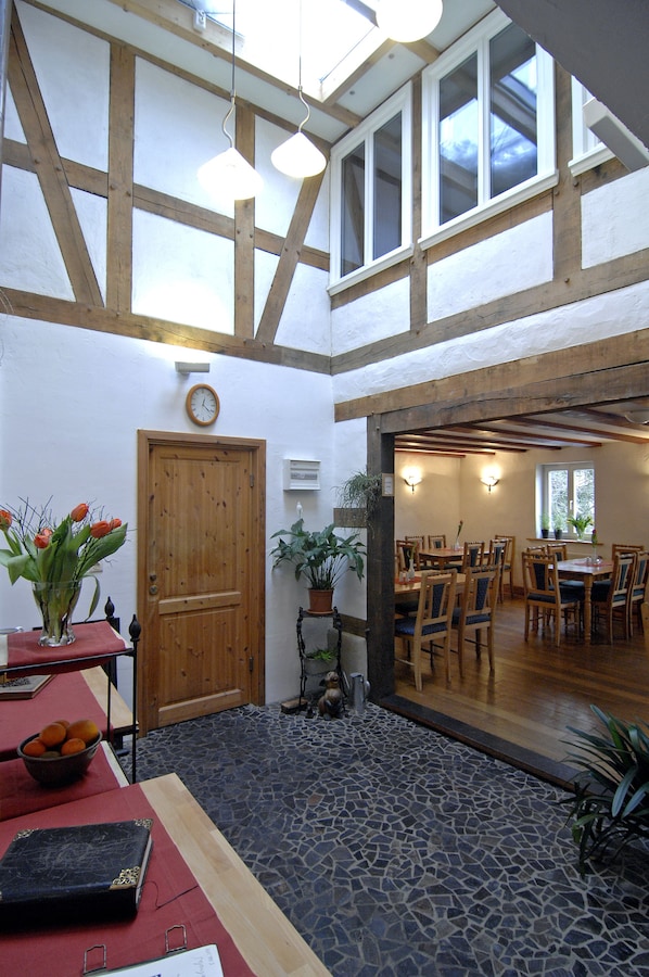 A dining area with wooden tables and chairs, a clock on the wall, and a door leading to another room.