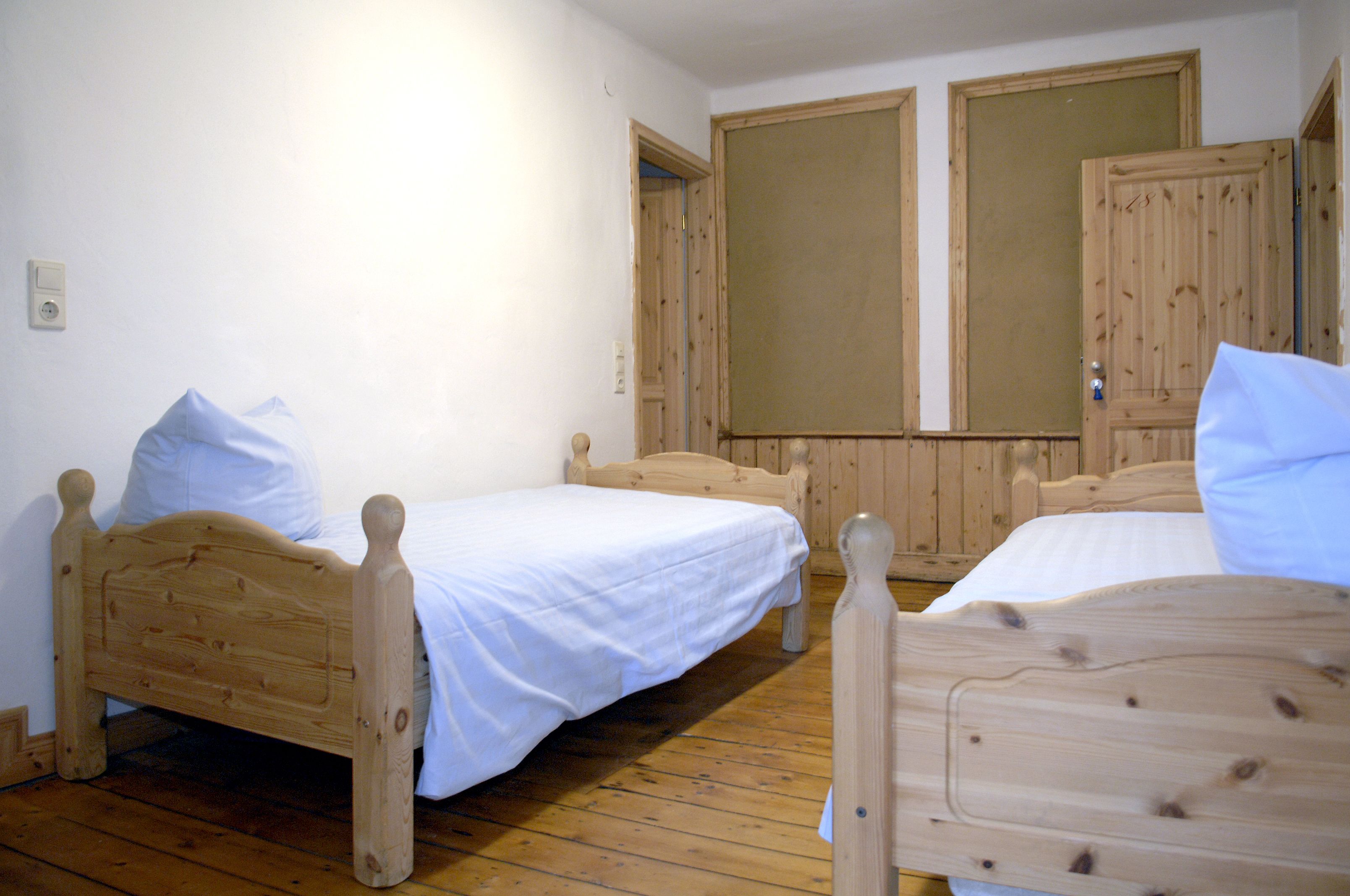 Una habitación con dos camas de madera, piso de madera y pared blanca.
