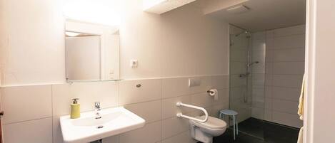 Un baño moderno con lavamanos, espejo e inodoro blancos.