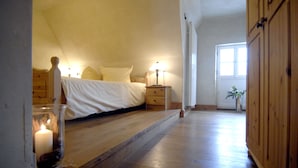 Un dormitorio con una cama, mesitas de noche, una mesilla y una ventana, además de una puerta.