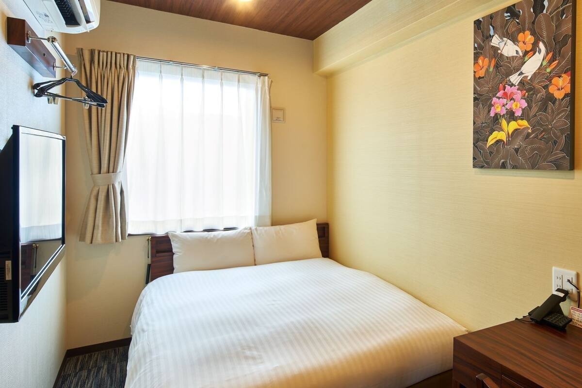 Ein Hotelzimmer mit Bett, Schreibtisch, Fernseher und einem Fenster mit Vorhängen.