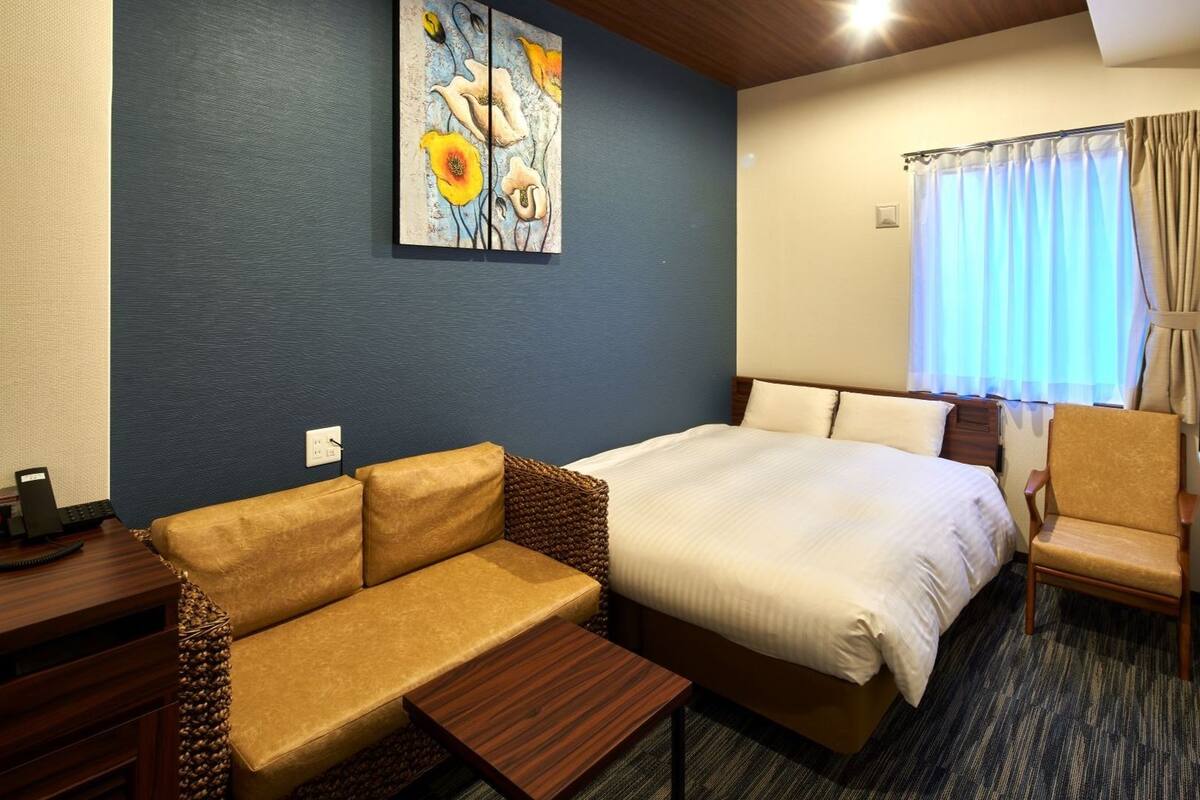 Ein Hotelzimmer mit Bett, Sofa, Sessel, kleinem Tisch und einem Bild an der Wand.