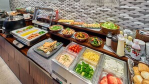 Ein reichhaltiges Buffet mit verschiedenen Speisen, darunter Obst, Gemüse und bereits zubereitete Gerichte.