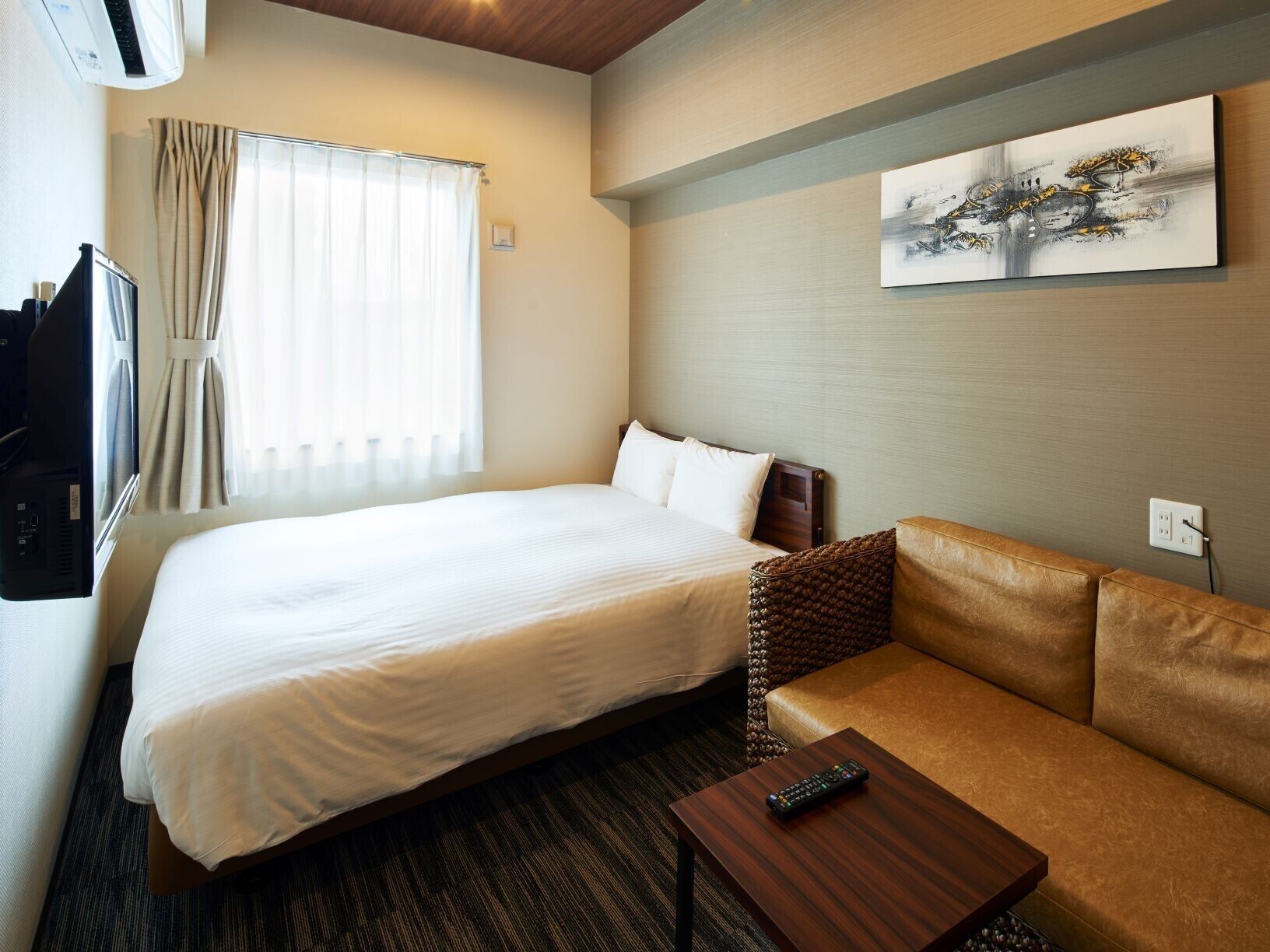 Ein Hotelzimmer mit Bett, Sofa, Fernseher und einem Gemälde an der Wand.