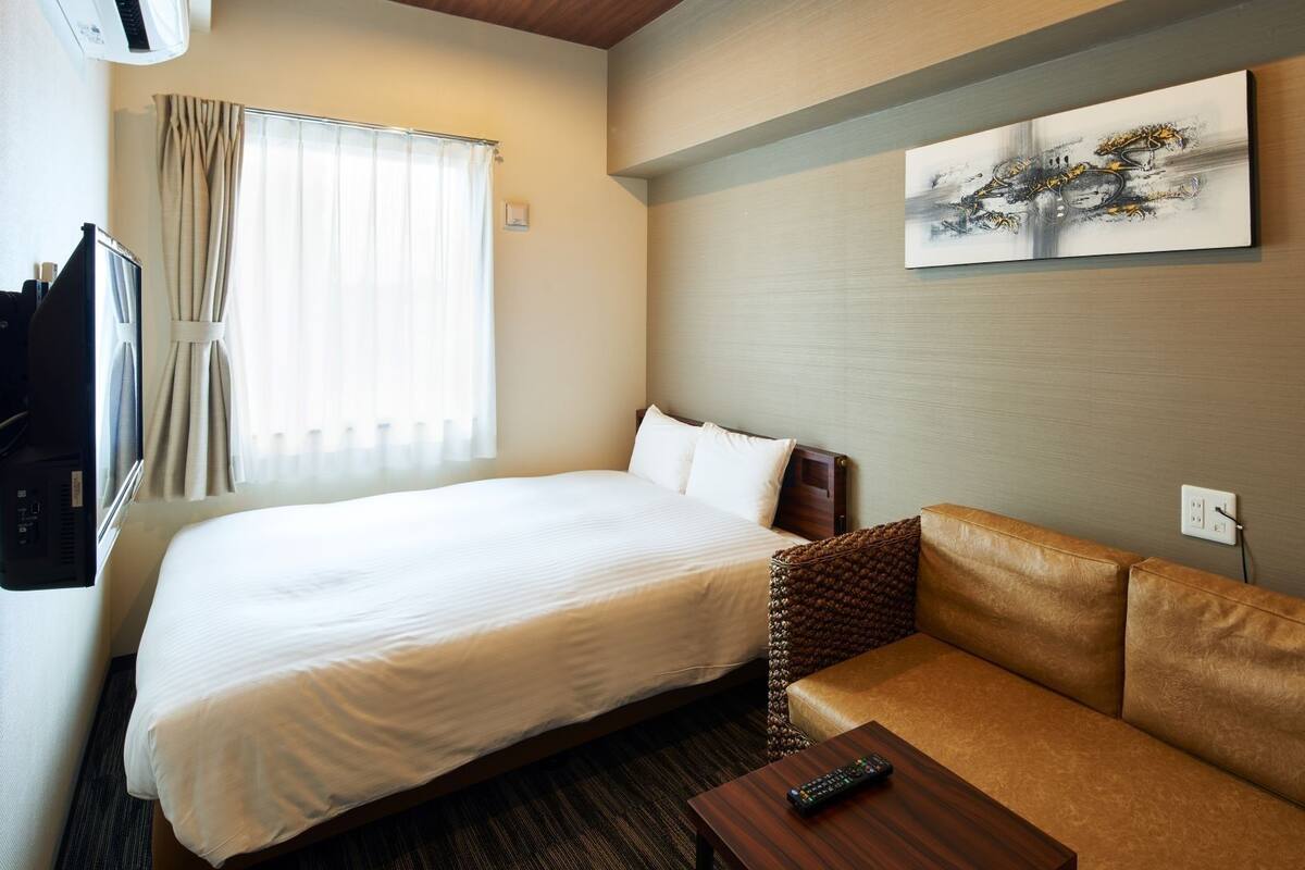 Ein Hotelzimmer mit Bett, Sofa, Fernseher und einem Gemälde an der Wand.