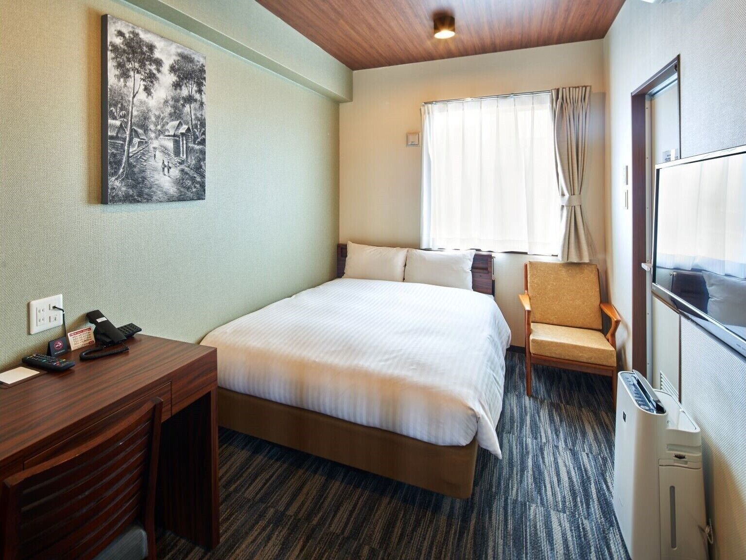 Ein Hotelzimmer mit Bett, Schreibtisch, Stuhl, Fenster mit Vorhängen und Heizkörper.
