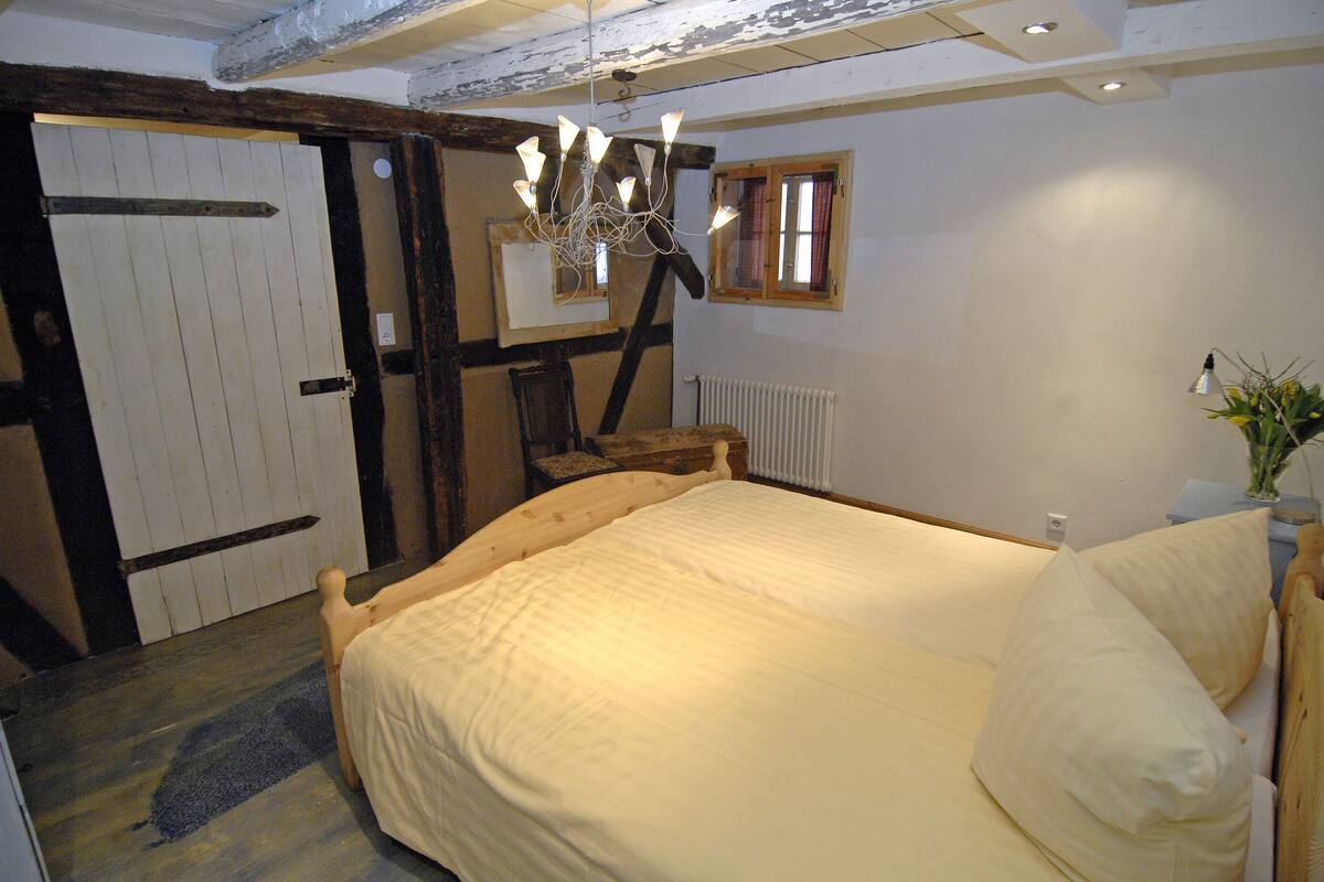 A bedroom with a wooden bed, a chandelier, a window with wooden shutters, and a radiator.