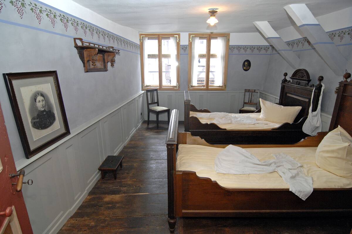 A room with two wooden beds, a chair, a small table, and a framed picture on the wall.