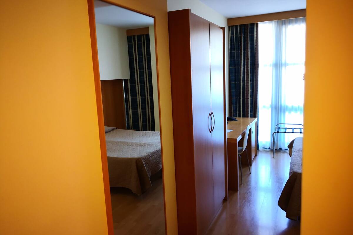 Habitación de hotel con cama, escritorio y silla. Se observa una ventana con cortinas.