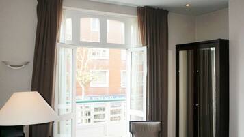 Une chambre d’hôtel équipée d’un bureau, d’une chaise et d’un lit. Elle comprend une fenêtre avec des rideaux, une porte et offre une vue sur l’extérieur.