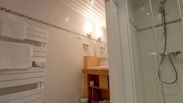 A bathroom with a glass-enclosed shower, white tiled walls, a wooden vanity, and a towel rack.