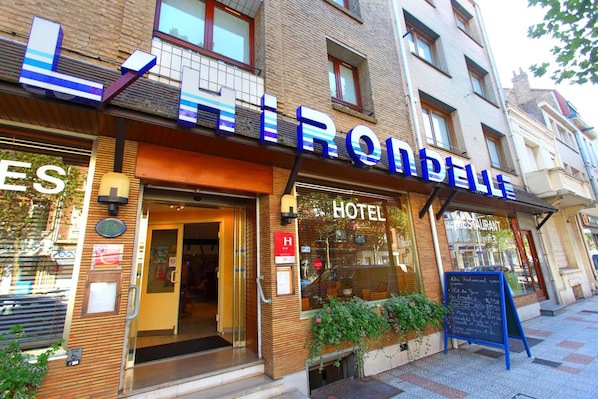 A hotel with a visible entrance, a signboard with room rates, and a restaurant sign.