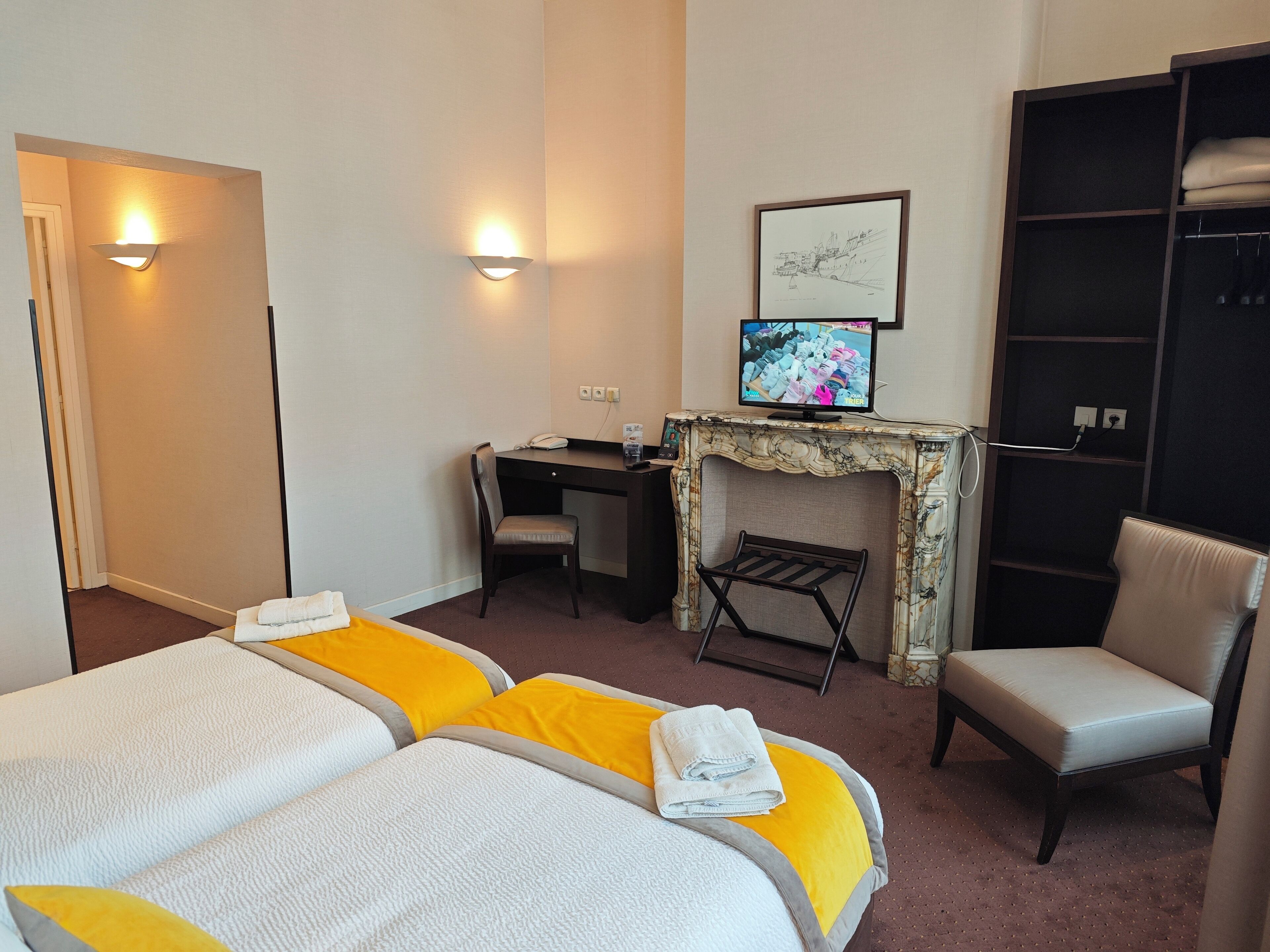 A hotel room with two beds, a desk, a chair, a television, and a wardrobe.