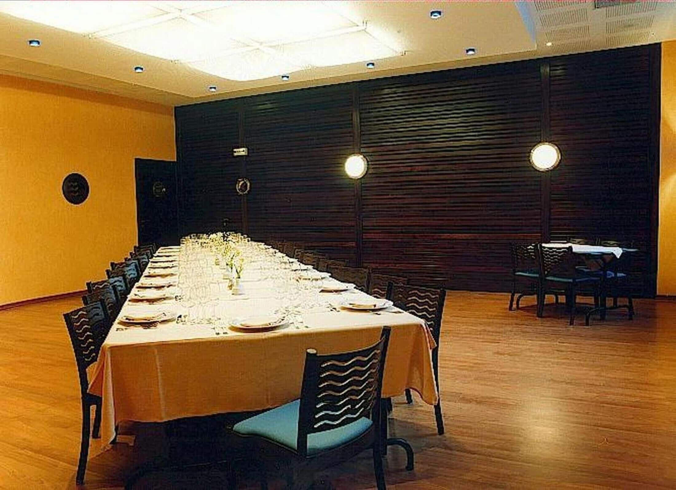 Un salón de conferencias con una larga mesa dispuesta para una reunión, equipado con sillas y un sistema de sonido.