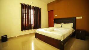 A neatly made bed with white linens and a rolled towel, a wooden headboard, a small bedside table, and a trash bin. - Kananam Retreat (Thodupuzha)