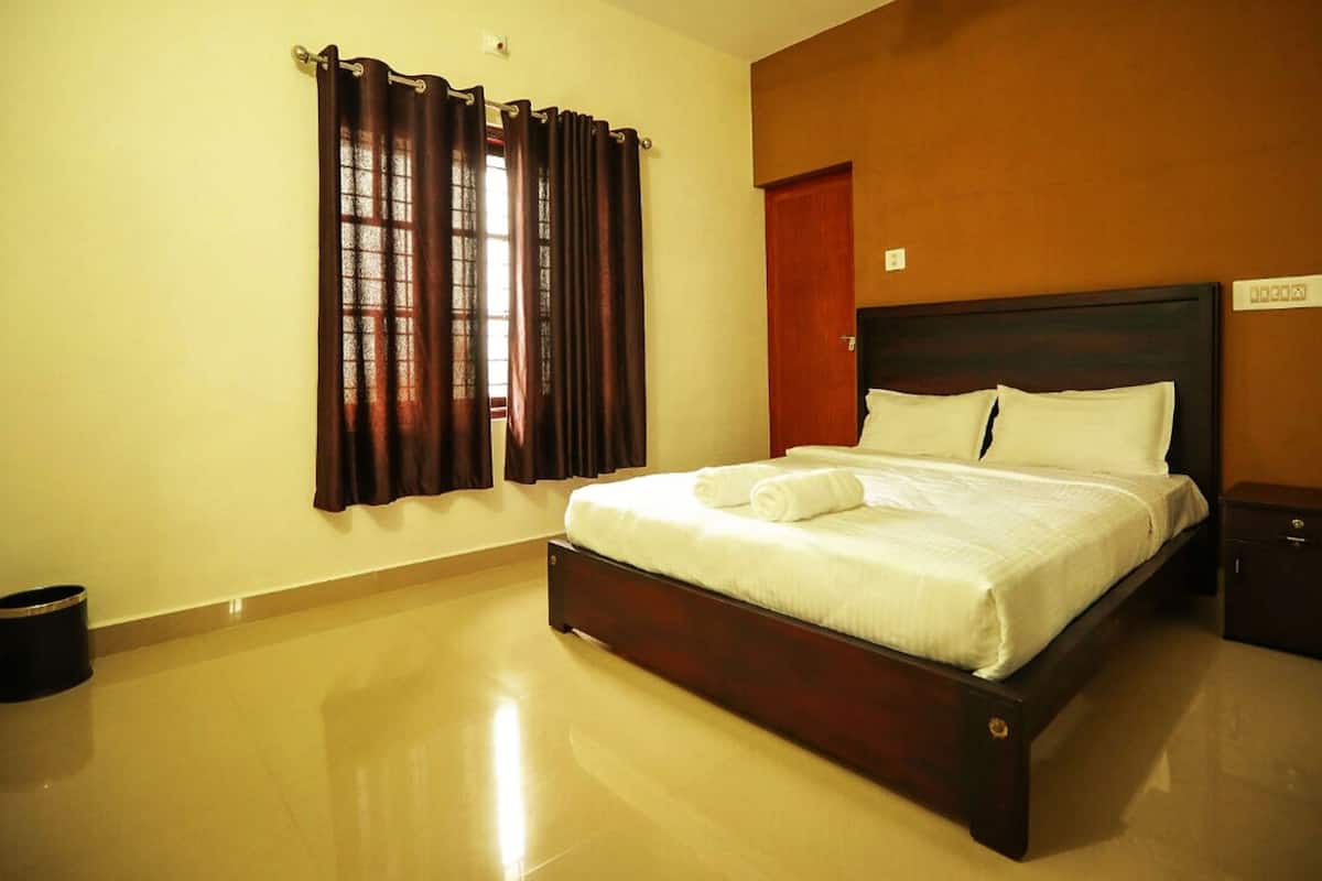 A neatly made bed with white linens and a rolled towel, a wooden headboard, a small bedside table, and a trash bin.