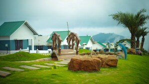 A resort with a grassy lawn, wooden bridge, and palm trees. - Kananam Retreat (Thodupuzha)