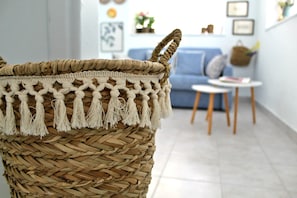 A woven basket with tassels in a room with a blue sofa, small round table, and framed pictures on the wall.