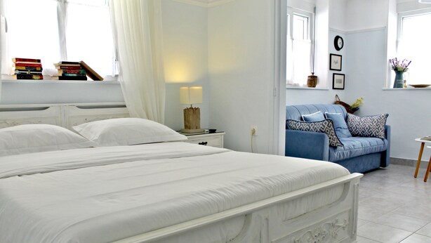 A bedroom with a large bed, a bedside table with a lamp, a blue sofa, and a window with curtains. - Nephiria, Under the Acropolis, In the heart of Plaka (Athens)