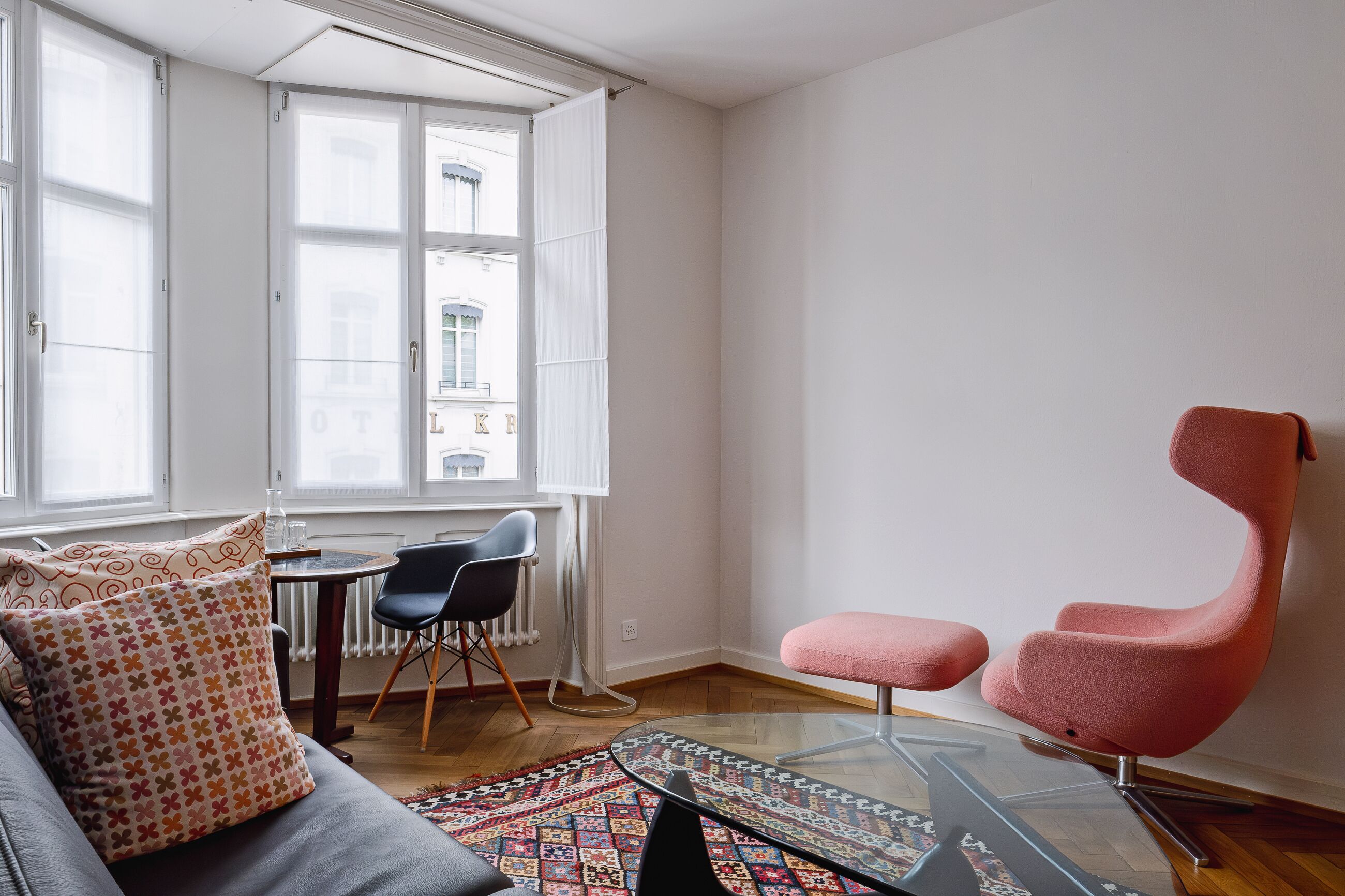 A modern living room with a glass coffee table, a pink armchair, and a sofa with patterned cushions.