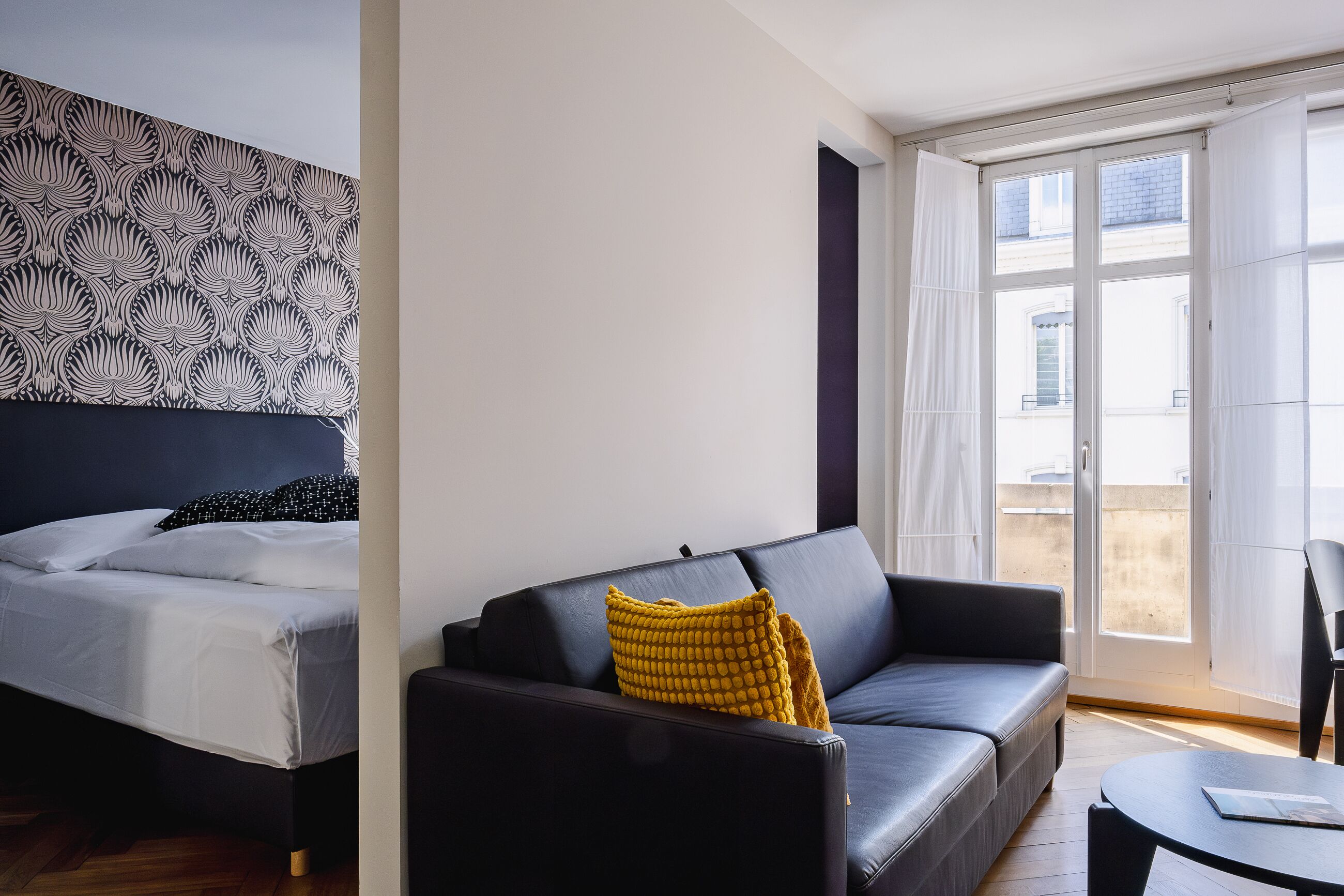A modern hotel room with a bed, a sofa, and a balcony with curtains.