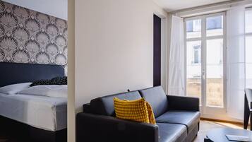 A modern hotel room with a bed, a sofa, and a balcony with curtains.