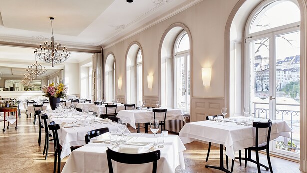 A dining area with tables set for service, large windows, and a chandelier. - Consum Boutique Hotel (Basel)