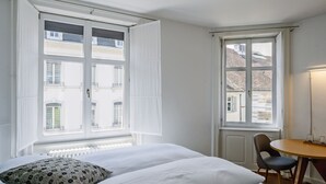 A hotel room with a bed, a chair, a table, and two windows. - Consum Boutique Hotel (Basel)