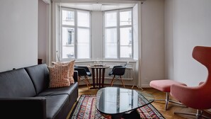 A modern living room with a black leather sofa, a pink armchair, a glass coffee table, and a patterned rug. - Consum Boutique Hotel (Basel)