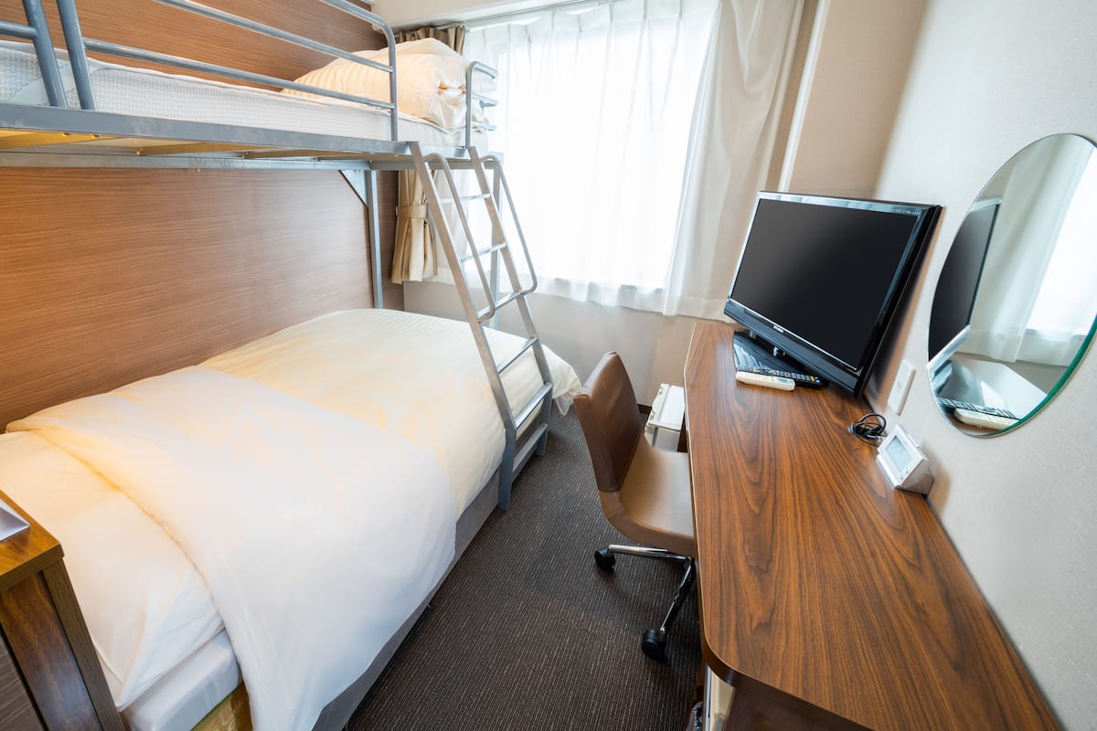 A hotel room with a bunk bed, a desk with a computer, and a TV.