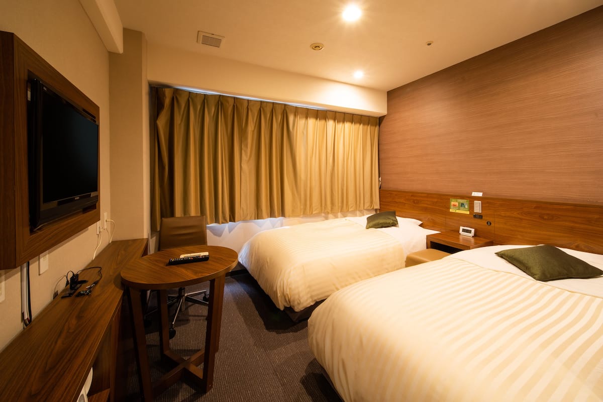 A hotel room with two beds, a TV, a desk, and a chair.