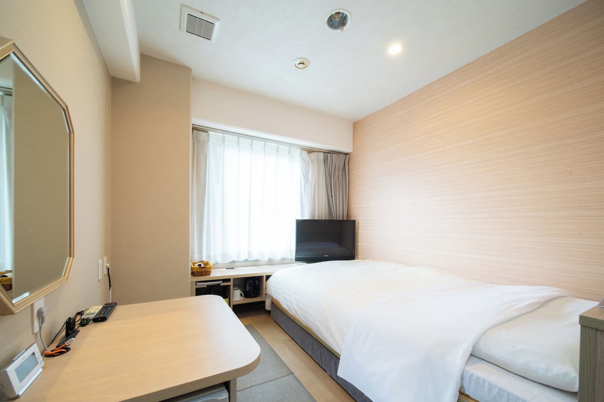 A hotel room with a bed, a TV, a desk with a microwave, and a window with curtains.