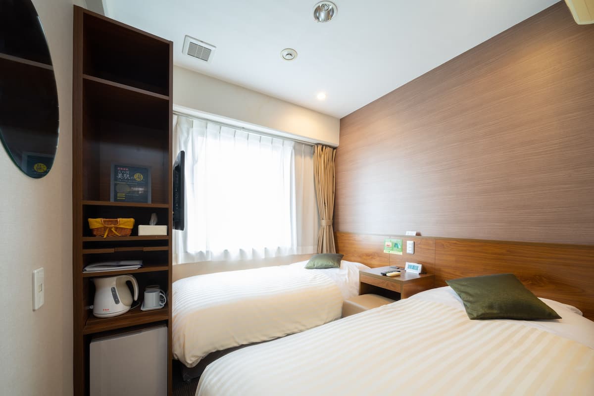 A hotel room with two beds, a minibar, a desk, and a window with curtains.